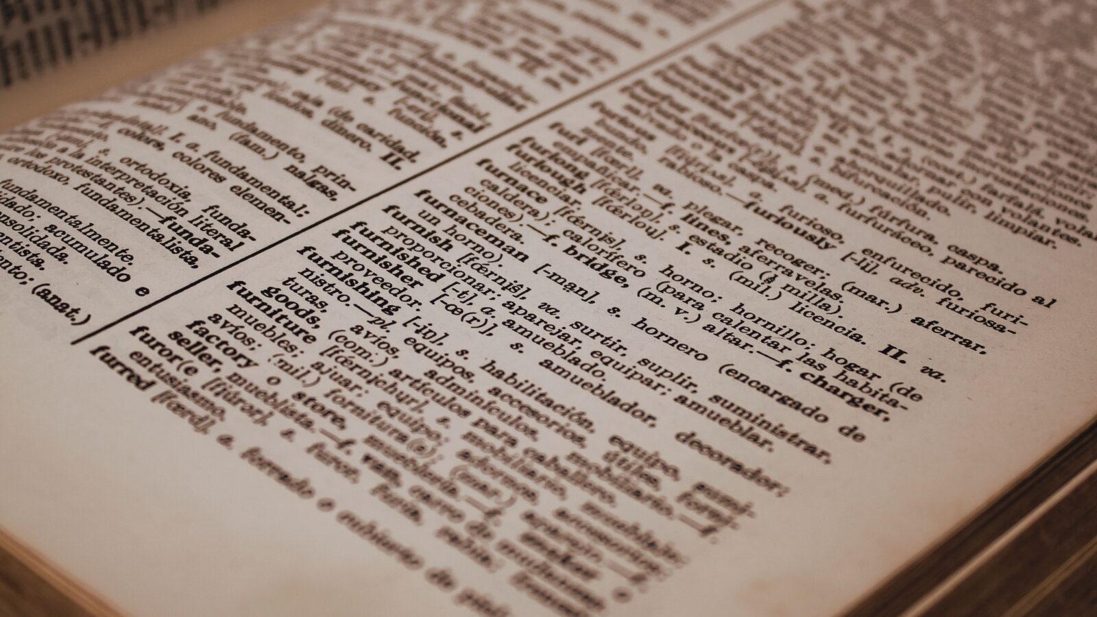 Open Spanish-English dictionary showing translated word pairs on a pink fabric background