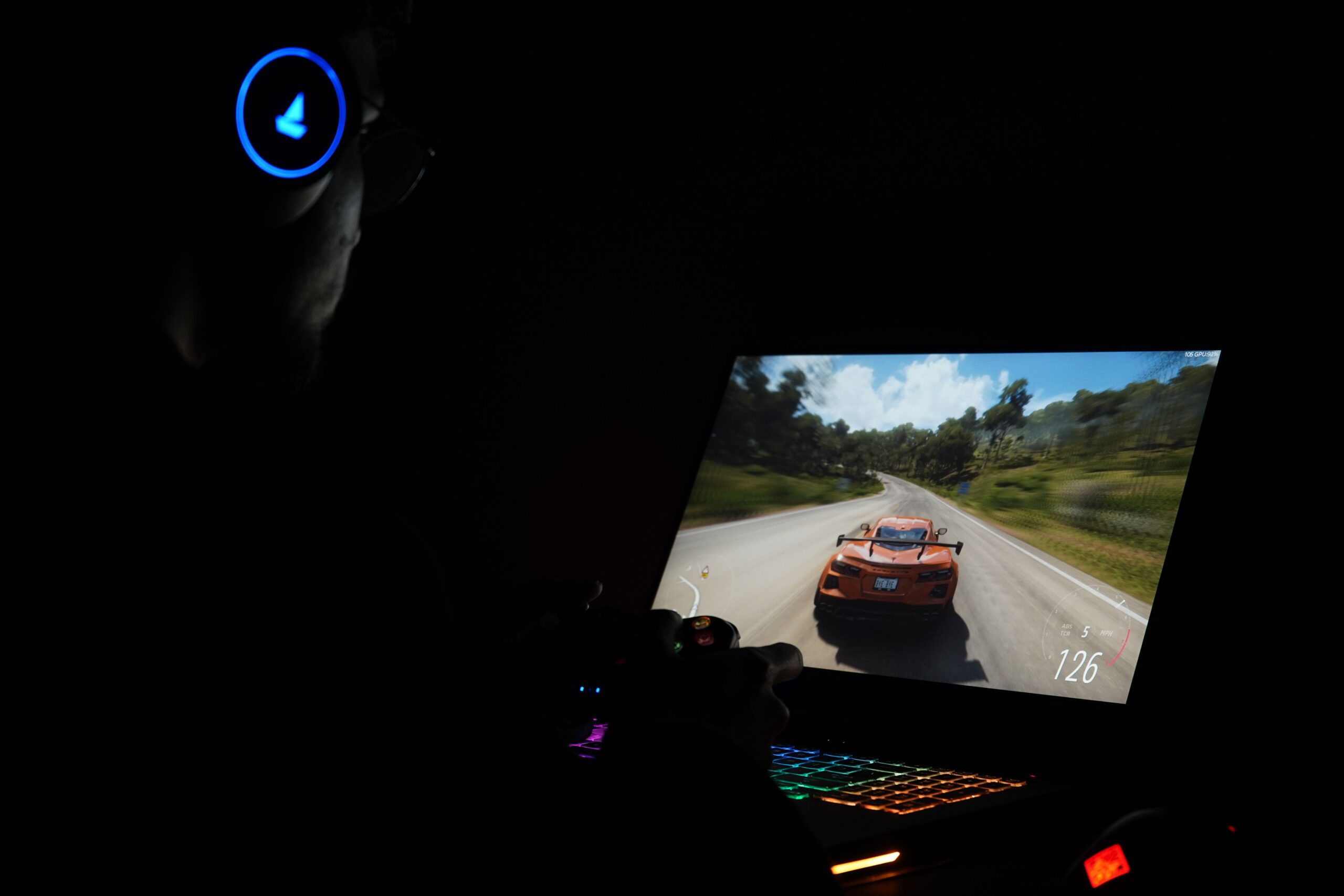 via Pexels, https://www.pexels.com/photo/man-in-headphones-sitting-in-the-darkness-and-playing-a-car-racing-game-on-a-laptop-15393003/ A gamer wearing headphones playing on a laptop, illustrating the busy Discord servers where translation noise matters most