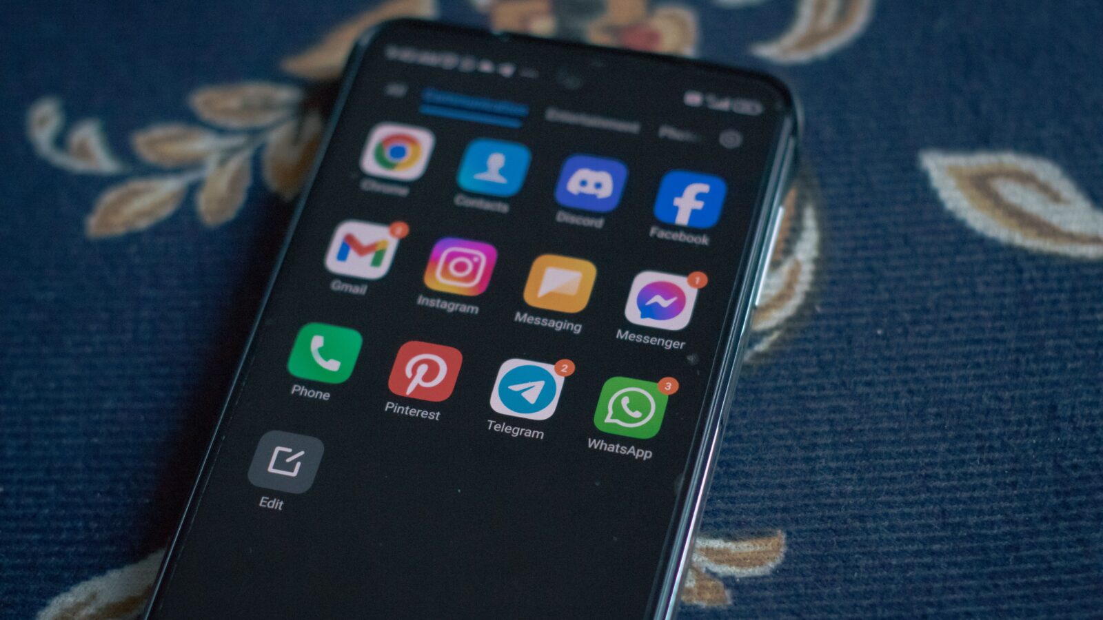 A smartphone on a blue cloth showing an app drawer that includes Discord among its messaging apps