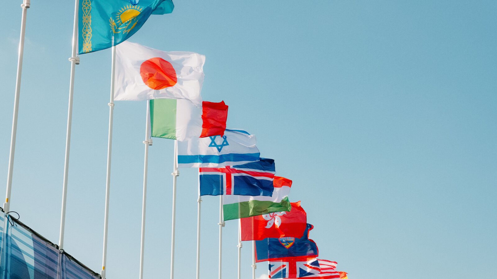 Rows of national flags on flagpoles against a clear blue sky, representing multilingual communities
