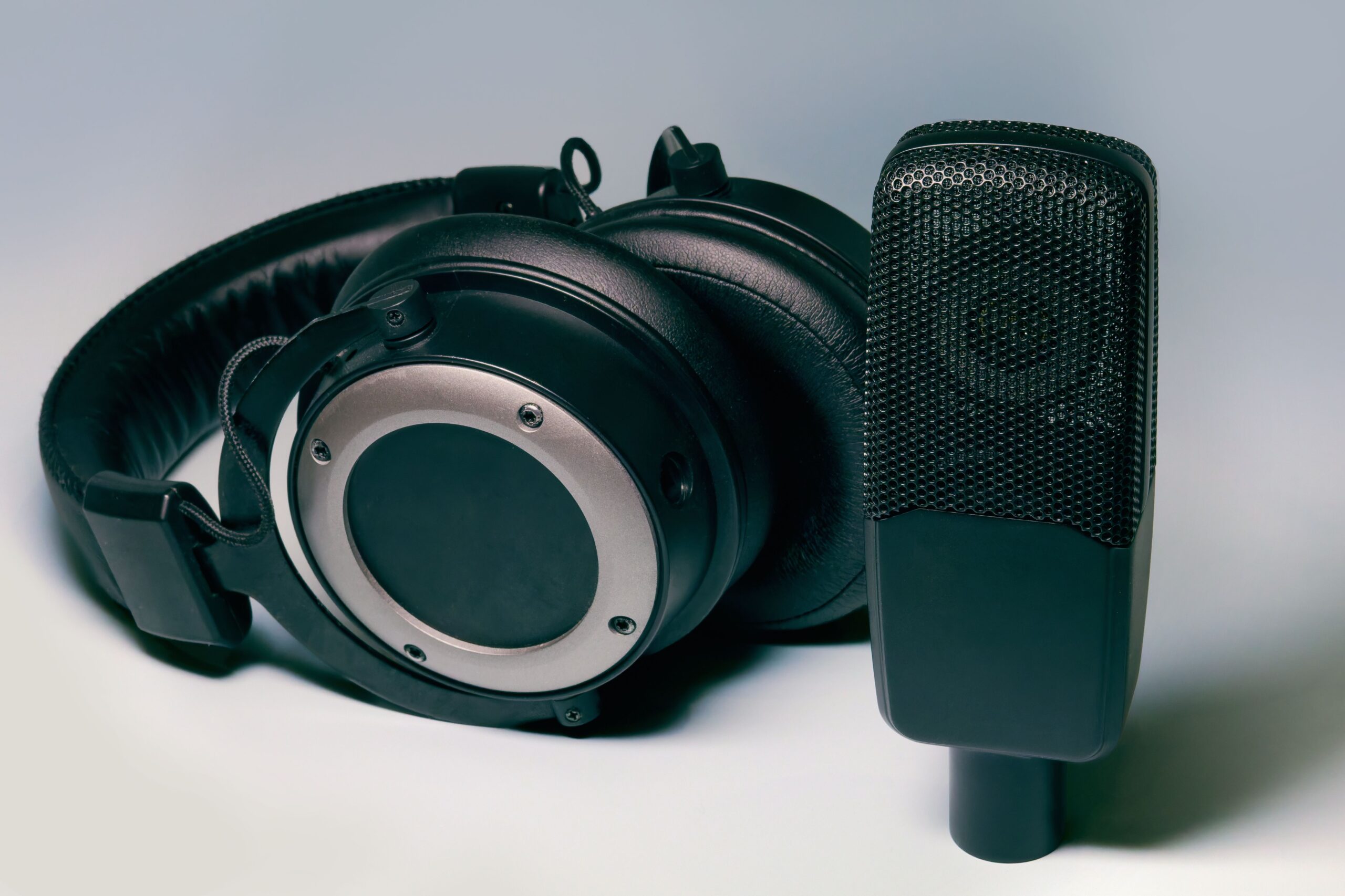 Black studio headphones beside a condenser microphone on a light surface