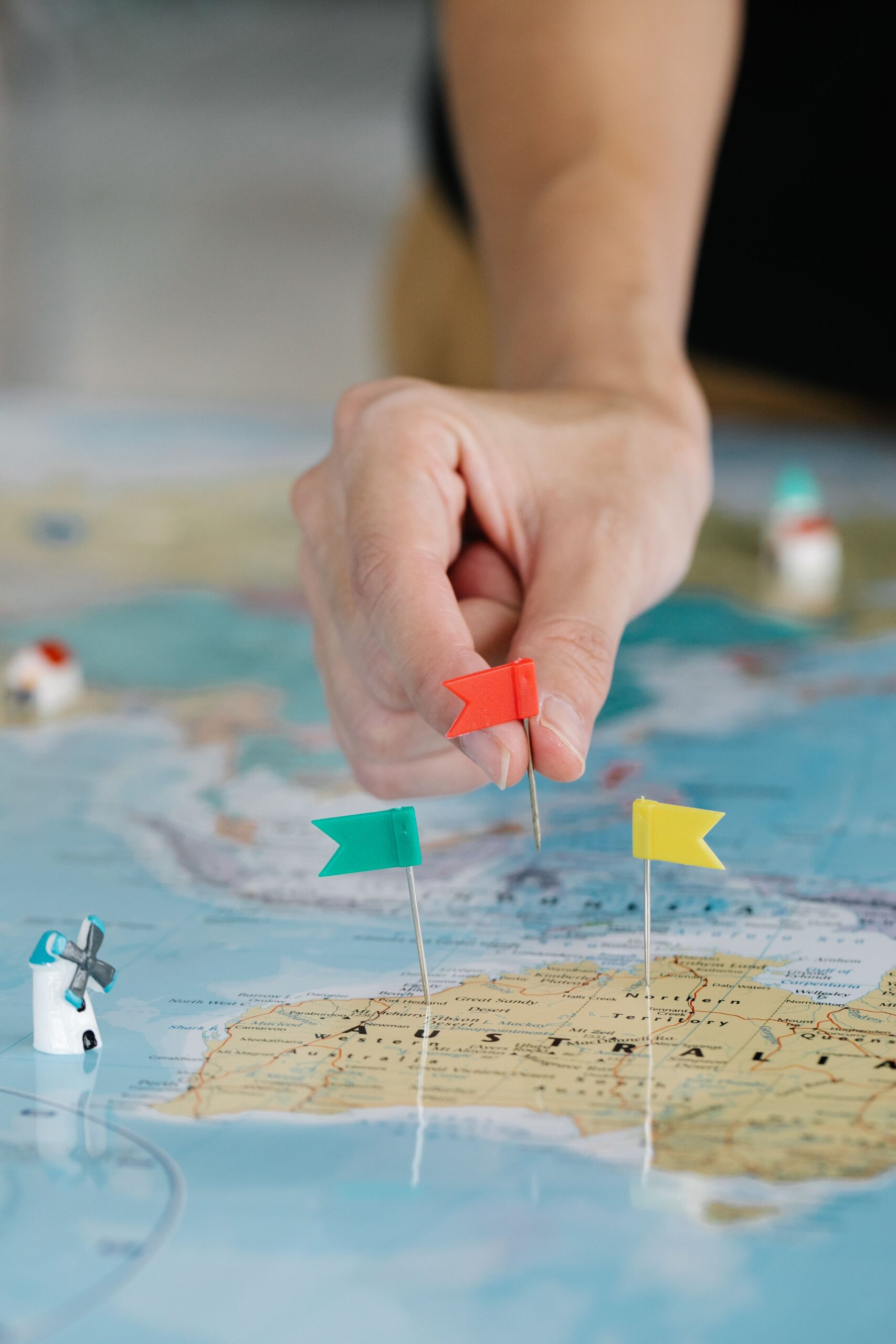 A hand places a small red country-flag pin on a world map already dotted with other flags