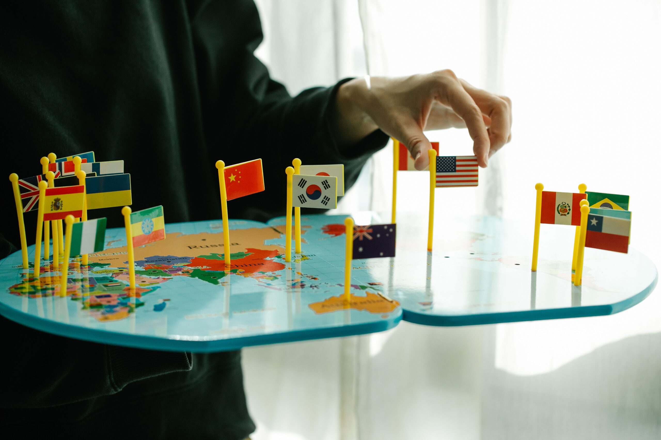 A hand placing a flag pin into an acrylic world map
