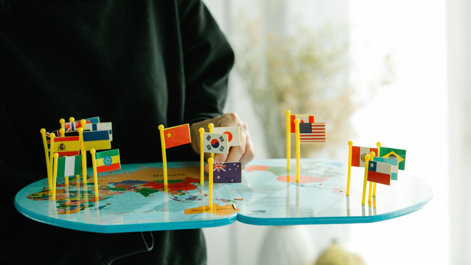 A hand holding a small round world map with many national flags pinned on it, each flag standing for one of the languages a Discord translator bot can handle